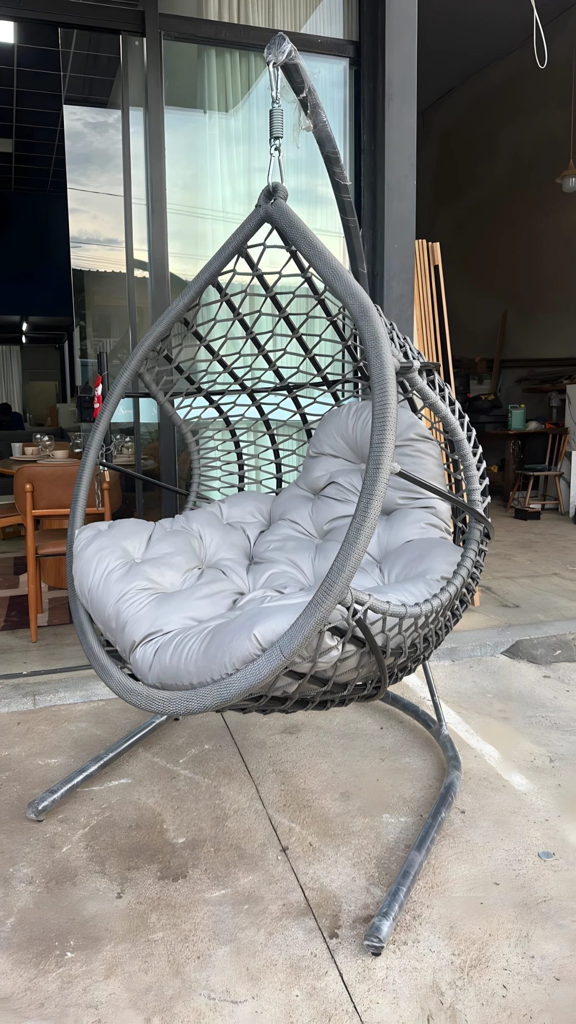 Poltrona suspensa em forma de gota com almofada cinza capitonê, em frente ao showroom