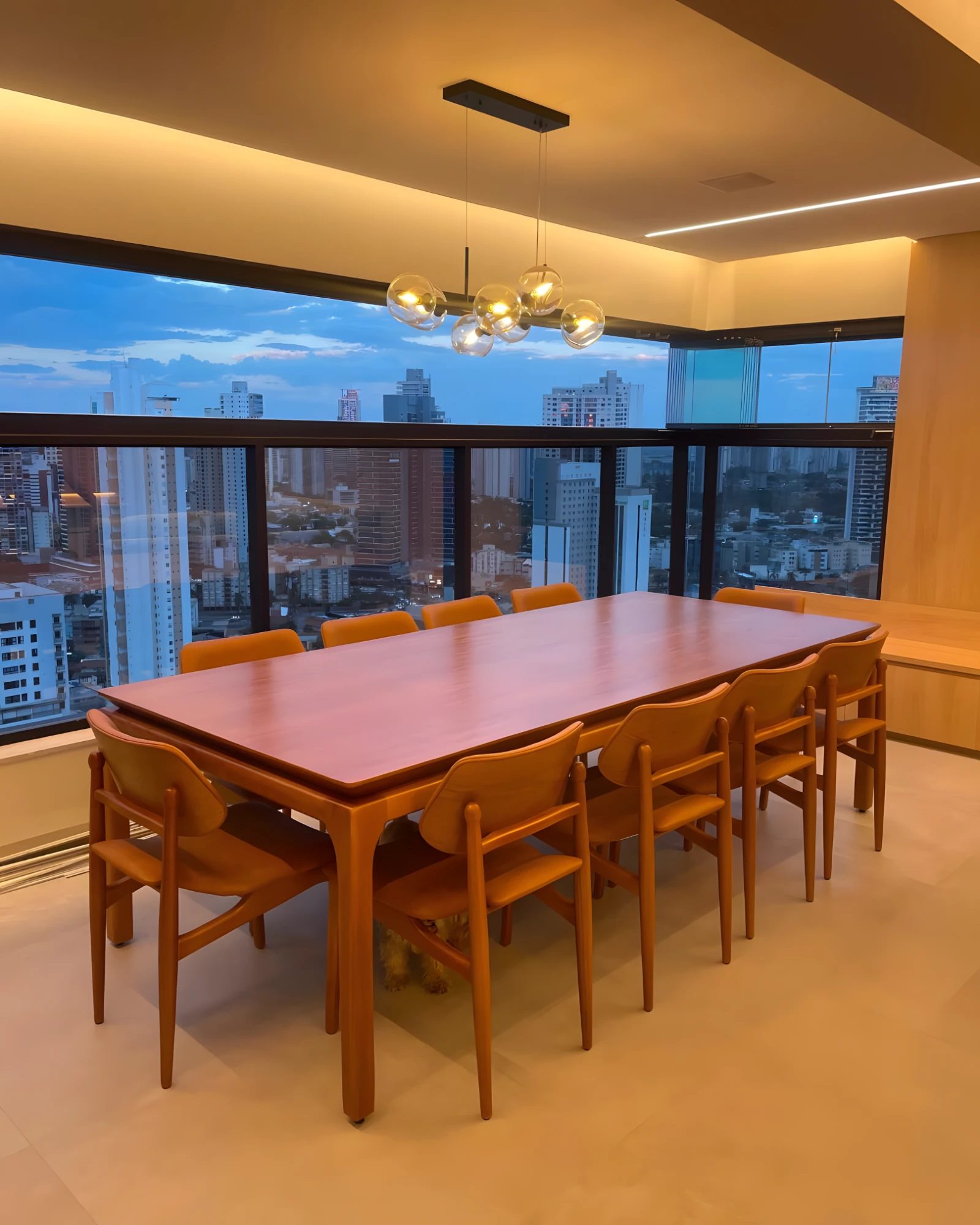 Mesa de jantar retangular em madeira com cadeiras de couro caramelo, em sala com vista para a cidade