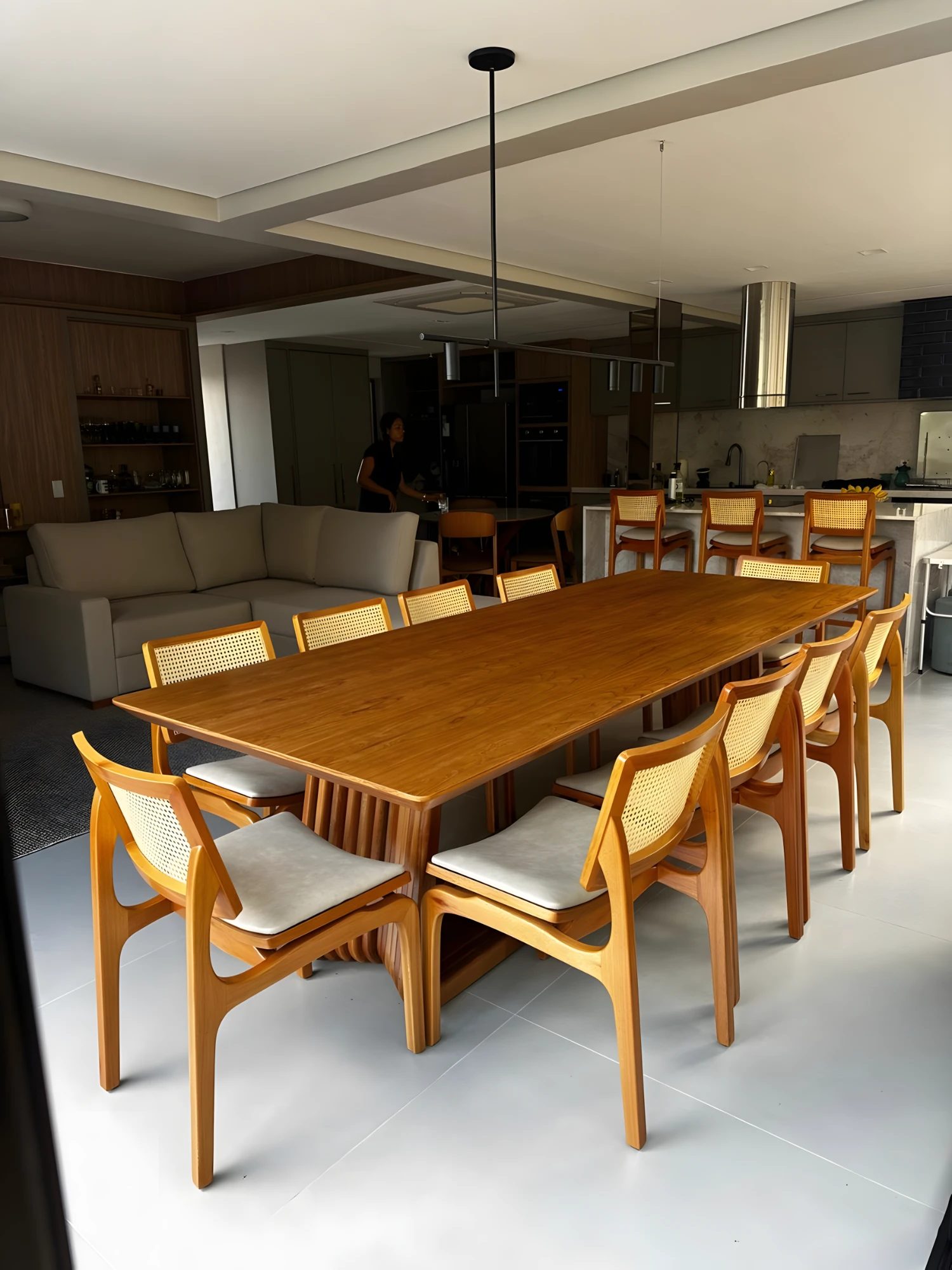 Mesa de jantar retangular em madeira com base ripada e cadeiras de palhinha com assento off-white, em sala integrada