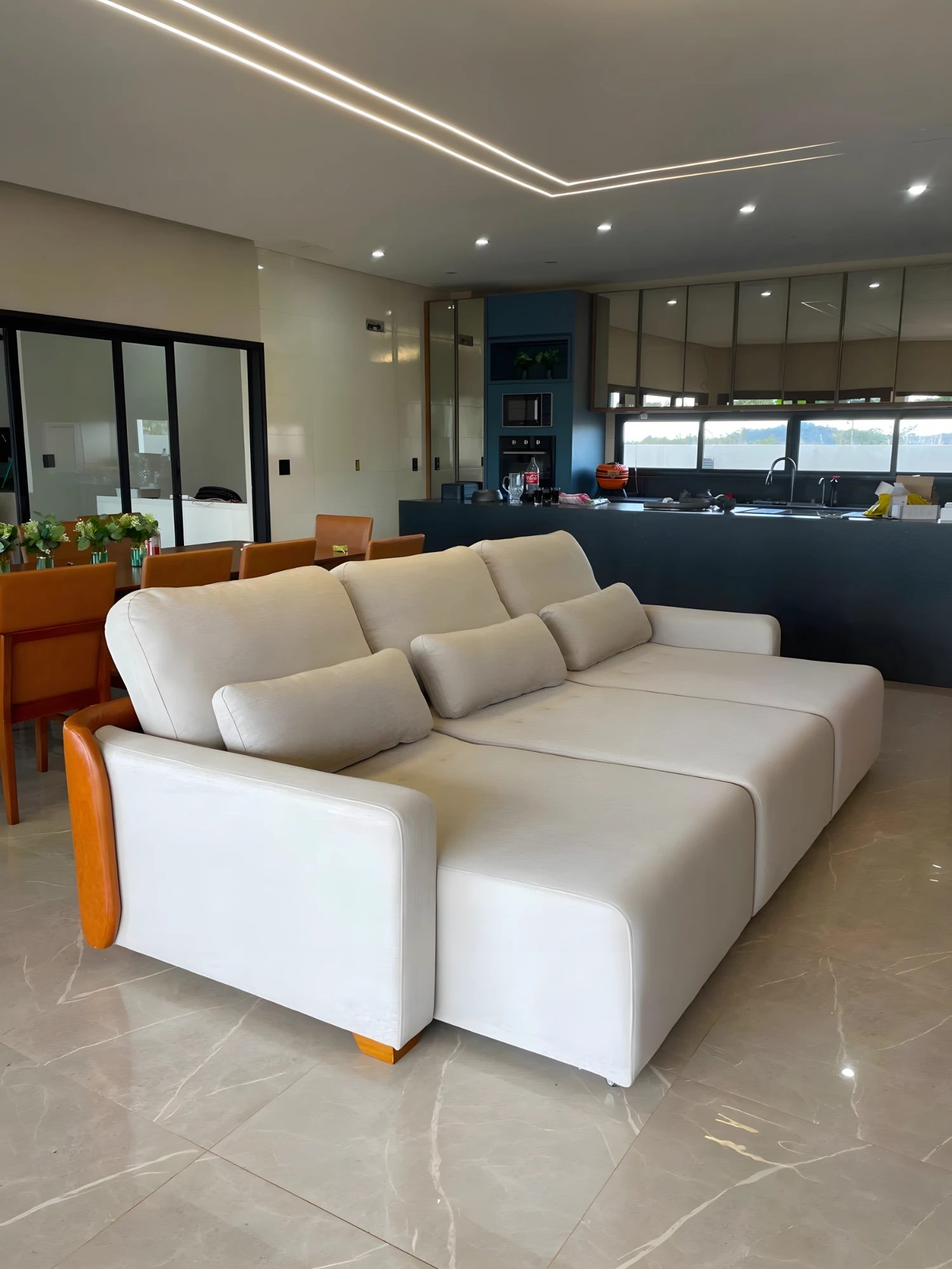Sofá retrátil off-white com braço em madeira em sala integrada à cozinha